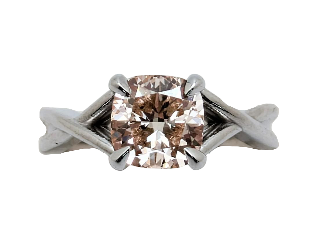 A pink diamond ring with a cushion-cut center stone, set in claw prongs in a silver-toned twisted shank, isolated on a white background.