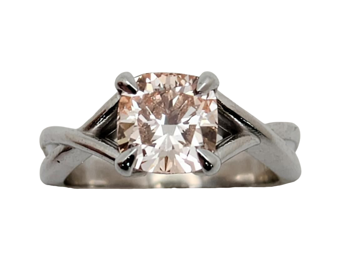 A pink diamond ring with a cushion-cut center stone, set in claw prongs in a silver-toned twisted shank, isolated on a white background, tilted slightly upwards.