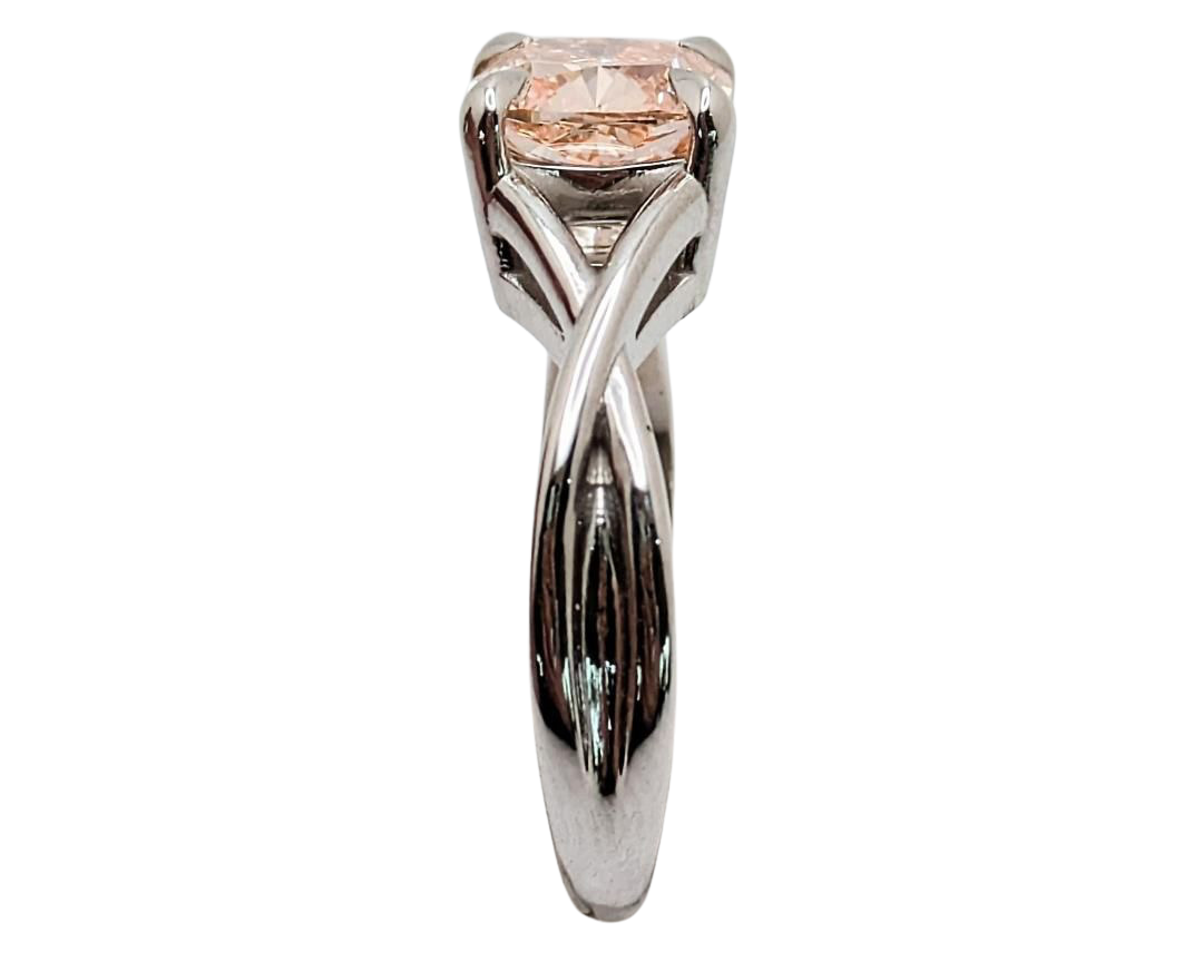 A pink diamond ring with a cushion-cut center stone, set in claw prongs in a silver-toned twisted shank, isolated on a white background, shown from the side.
