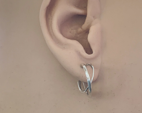 A pair of polished silver-toned open hoop earrings with a modern, flowing curved design, displayed on an ear model.