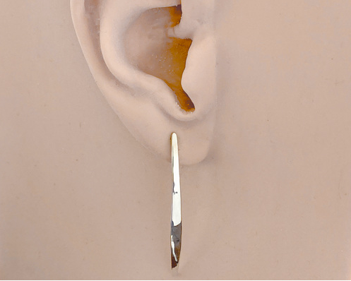 A pair of polished silver long curved post earrings, shown on an ear model.