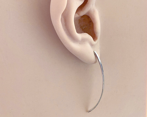 A pair of polished silver long curved post earrings, shown on an ear model facing slightly sideways to show curve.