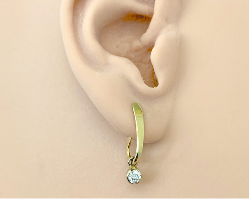 A pair of gold post 'j-hoop' earrings with a small round diamond dangling from the bottom, shown on ear.